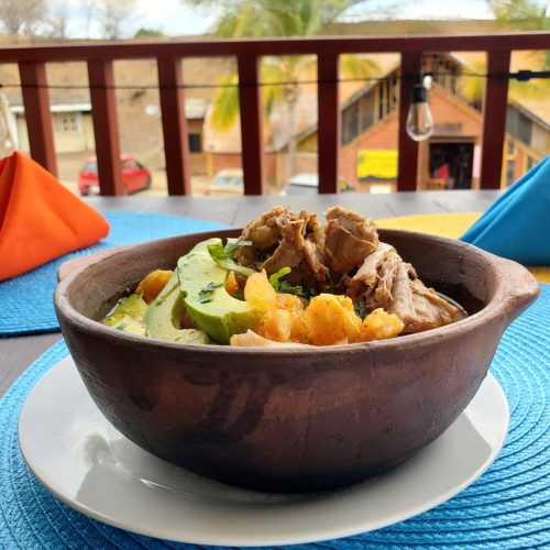 Guiso de cerdo con mote y aguacate servido en plato de barro artesanal en la cafetería Nia Kapro
